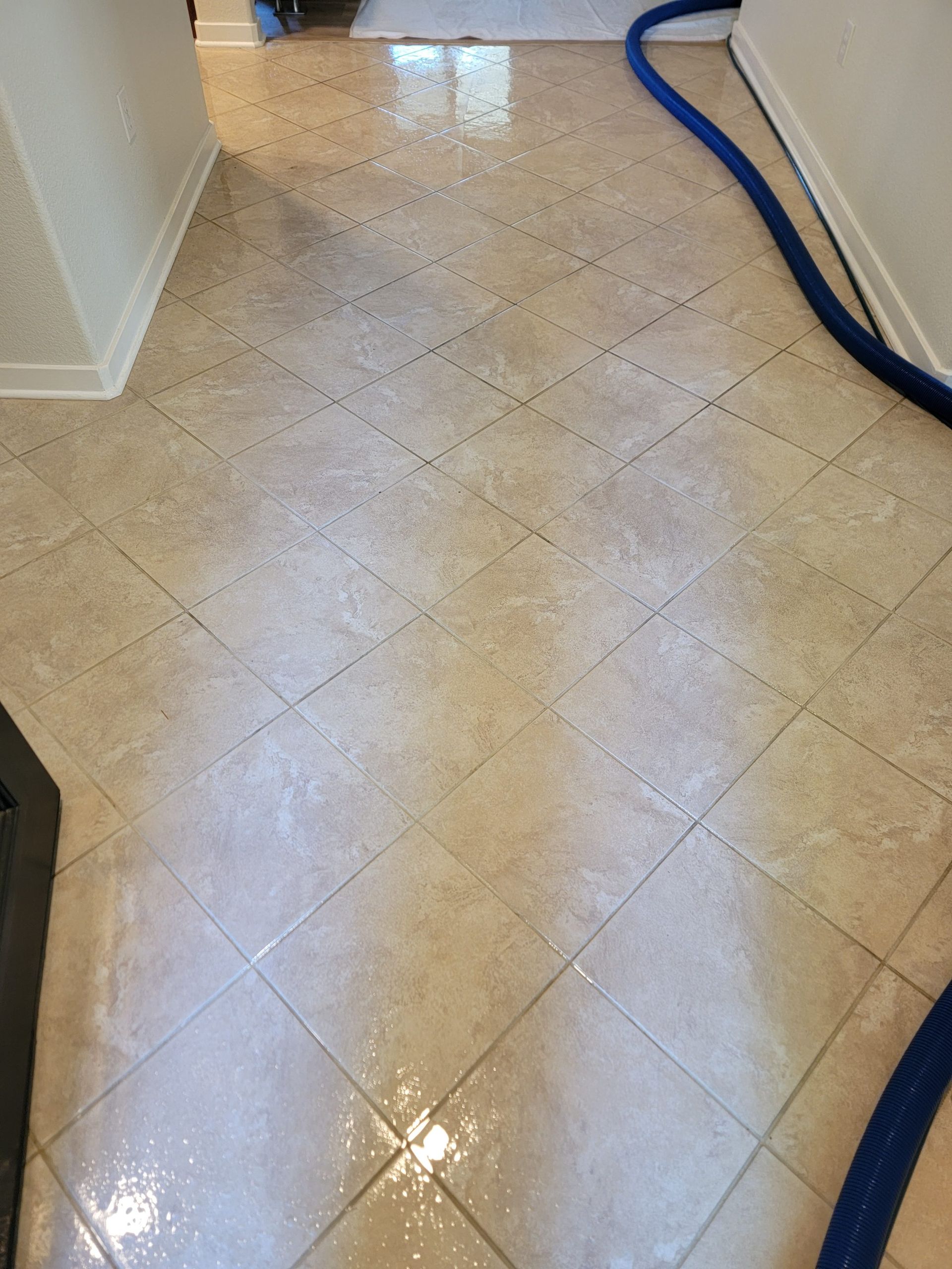 Shiny beige tiled hallway floor with a blue hose or cable along the right wall