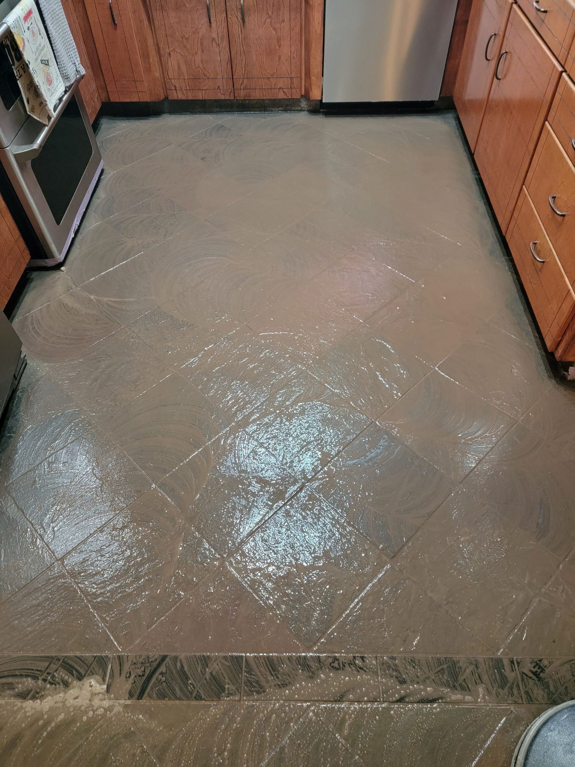 Kitchen floor with a large wet spill, surrounded by wooden cabinets and appliances