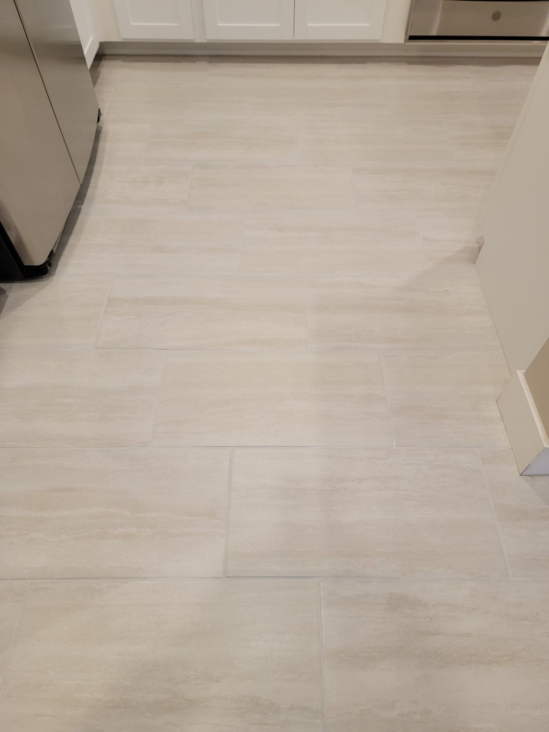 A top-down view of light, neutral-toned rectangular tile flooring in a kitchen setting.
