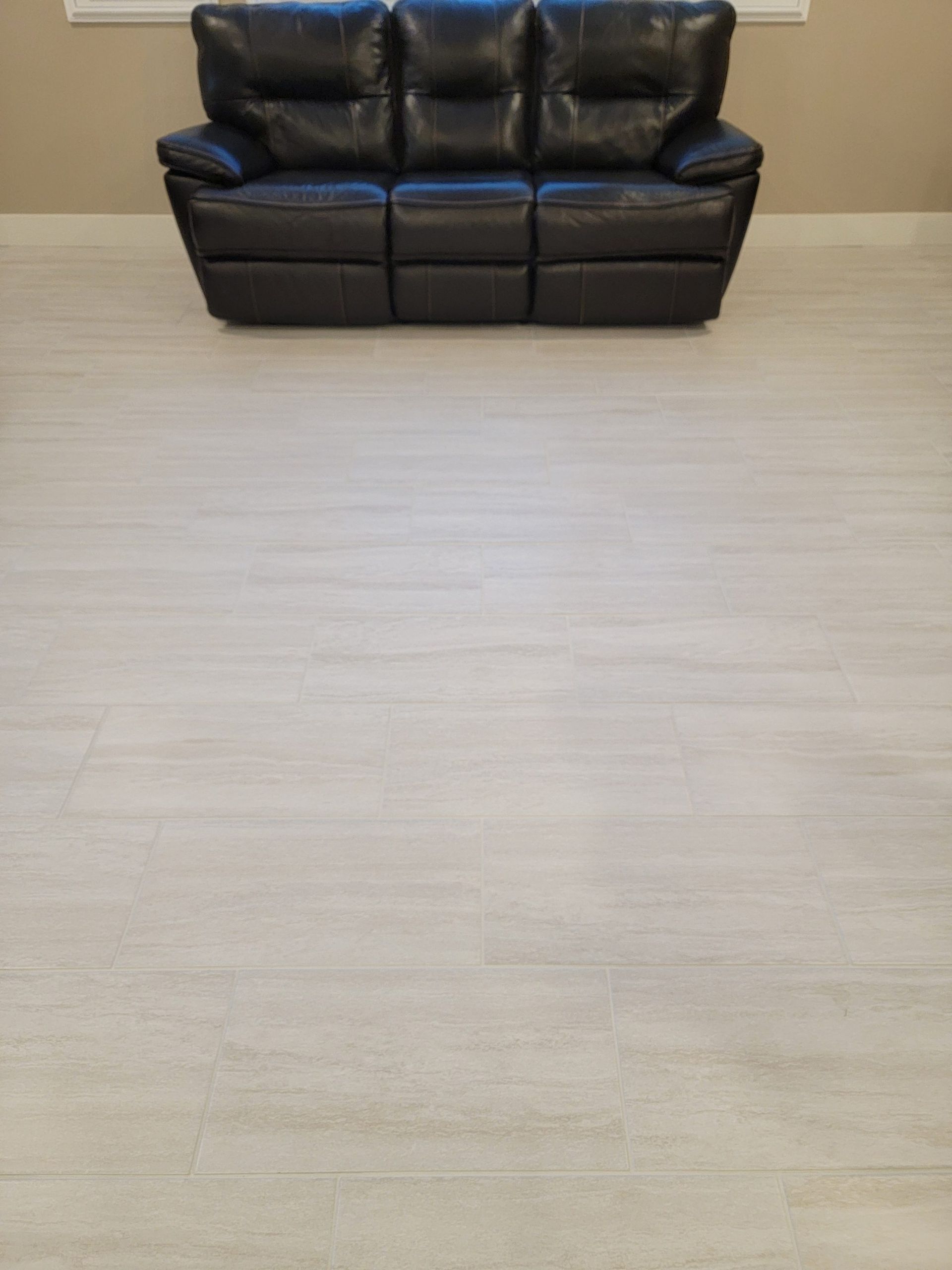 A dark brown leather sofa centered against a plain wall on a light-colored, wood-look floor.
