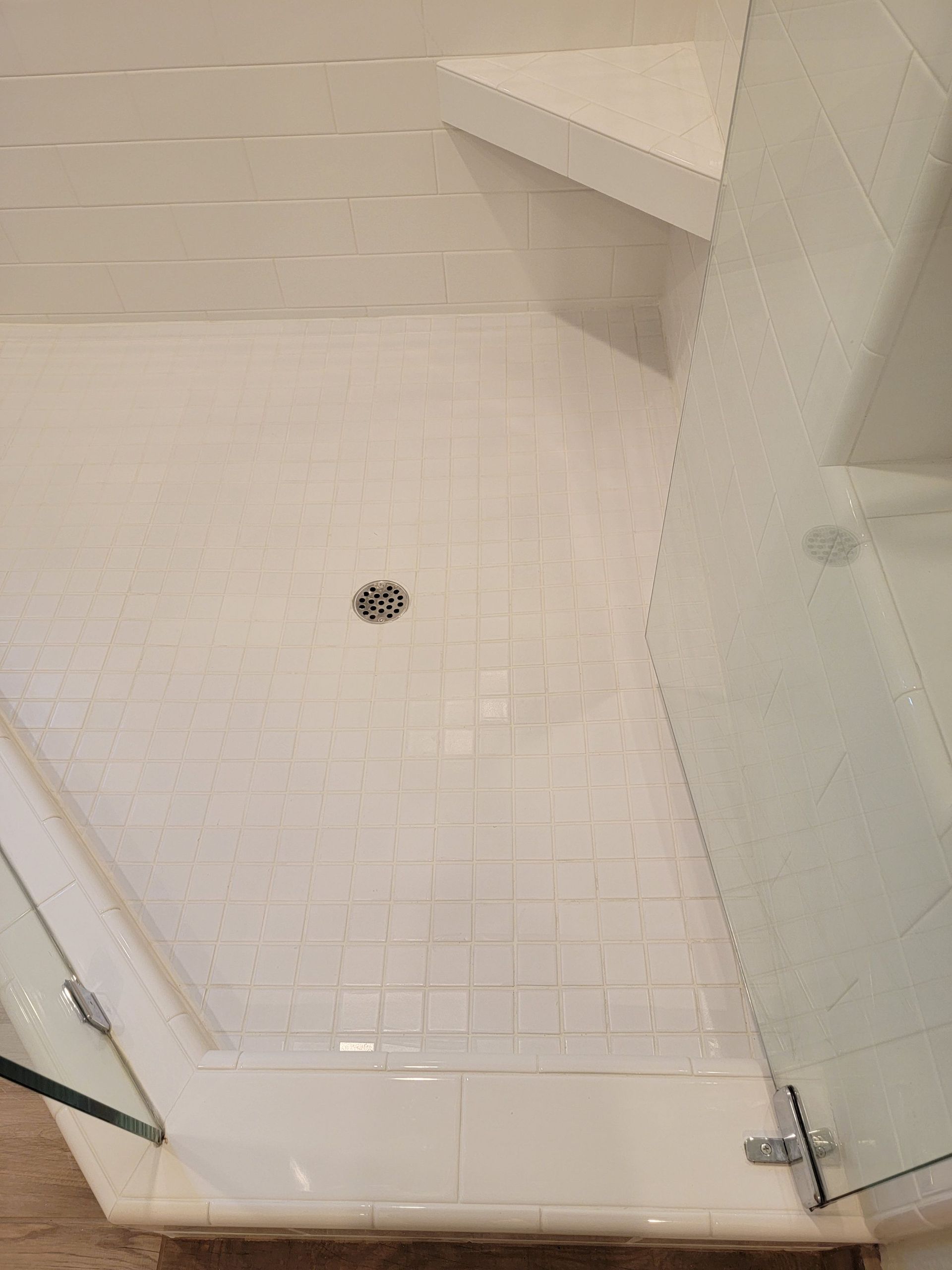 A white-tiled shower stall with a corner bench, glass door, and center drain.