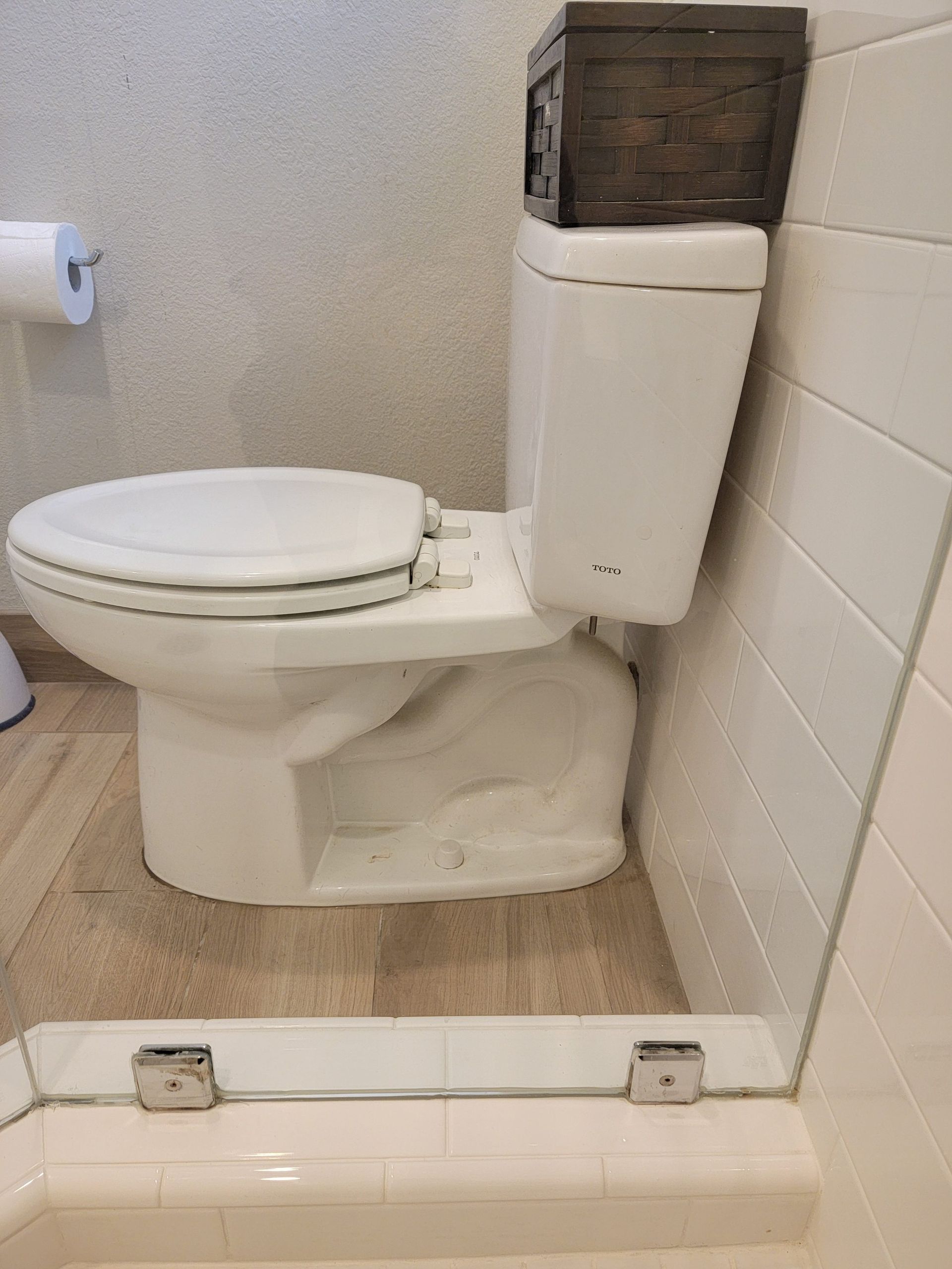 A white toilet in a bathroom, with a dark woven basket resting on top of the tank.