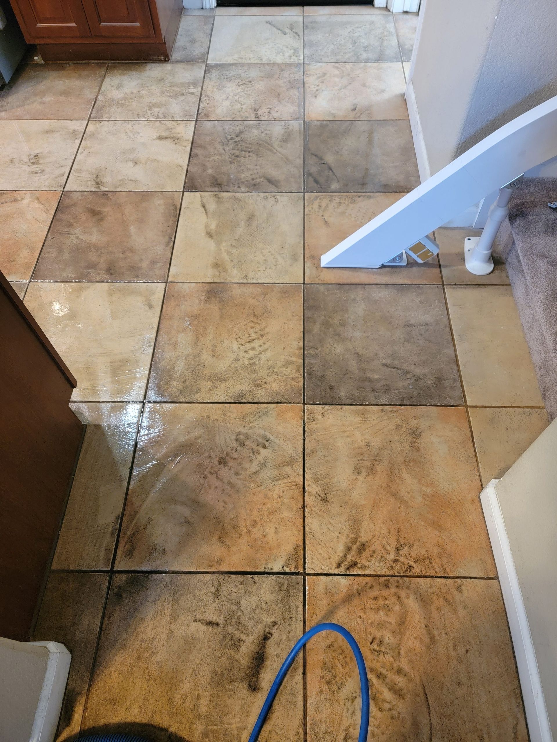 Top-down view of textured, square stone floor tiles in a home, with some areas showing signs of cleaning or moisture.
