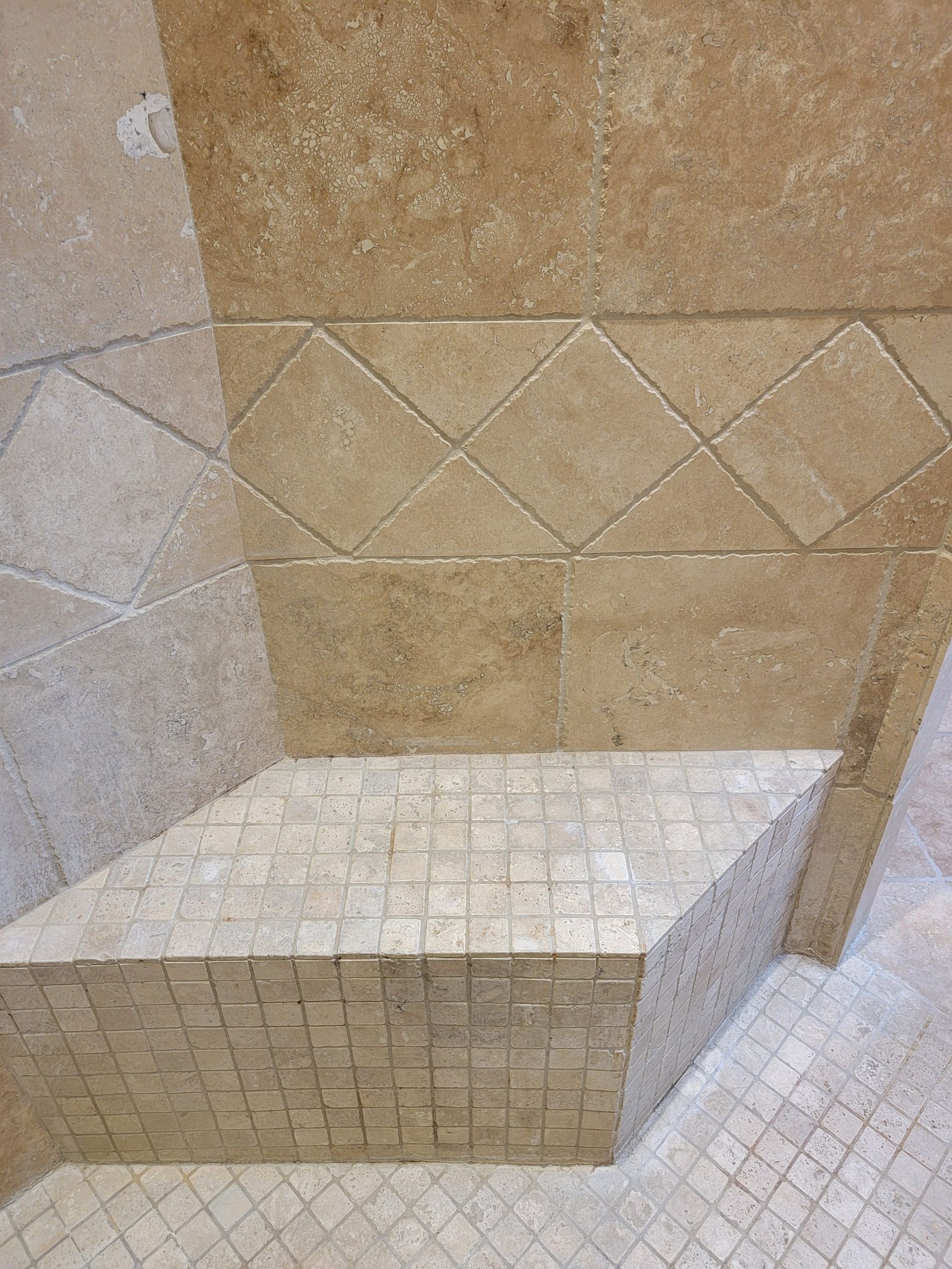 A corner shower with beige tile walls, a decorative diamond-patterned accent border, and a tiled built-in seat.