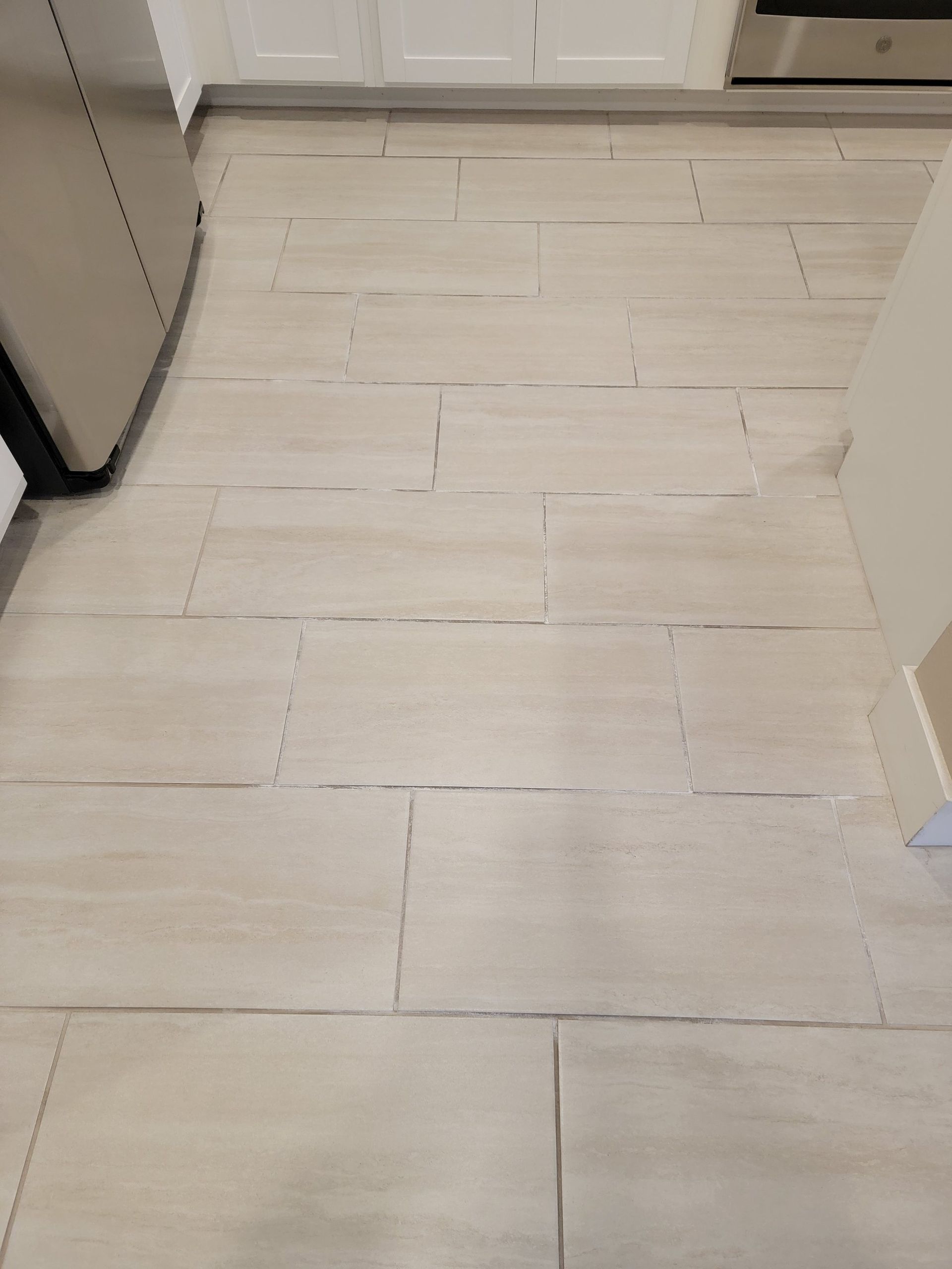 A kitchen floor featuring light, rectangular stone-look tiles laid in a standard running bond pattern.