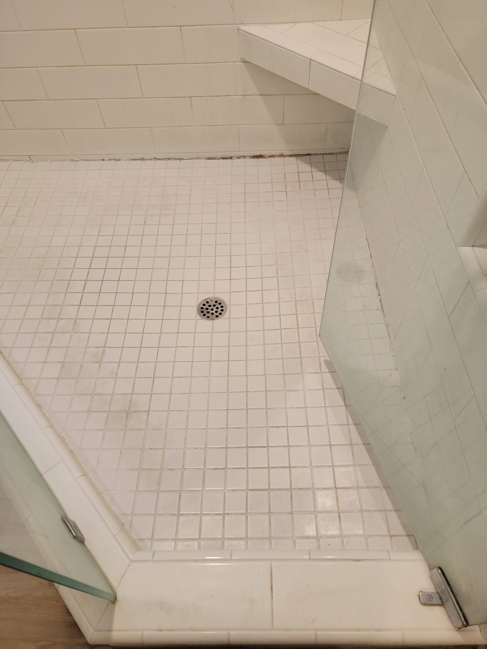 A walk-in shower with white square floor tiles, a built-in corner bench, and a glass door.