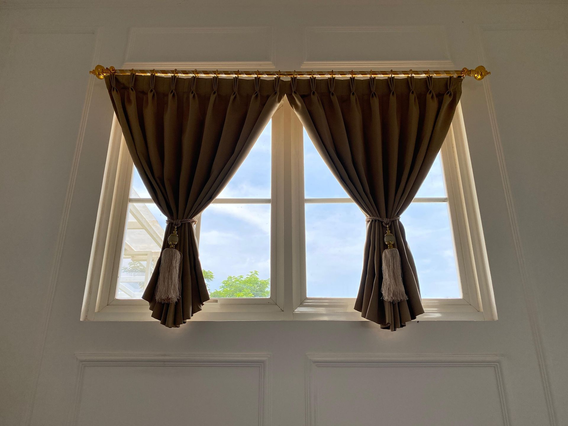 White sheer curtains hanging in front of a window, with wavy lower edge over a wooden floor.