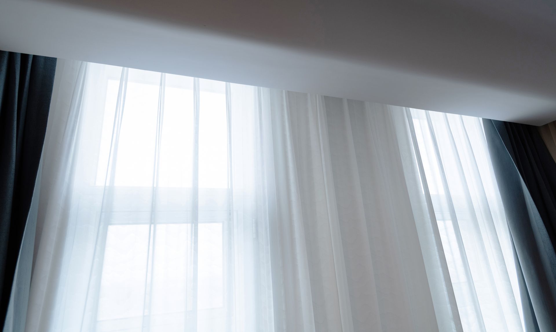 Sheer white curtains and dark gray drapes framing a window, filtering light.