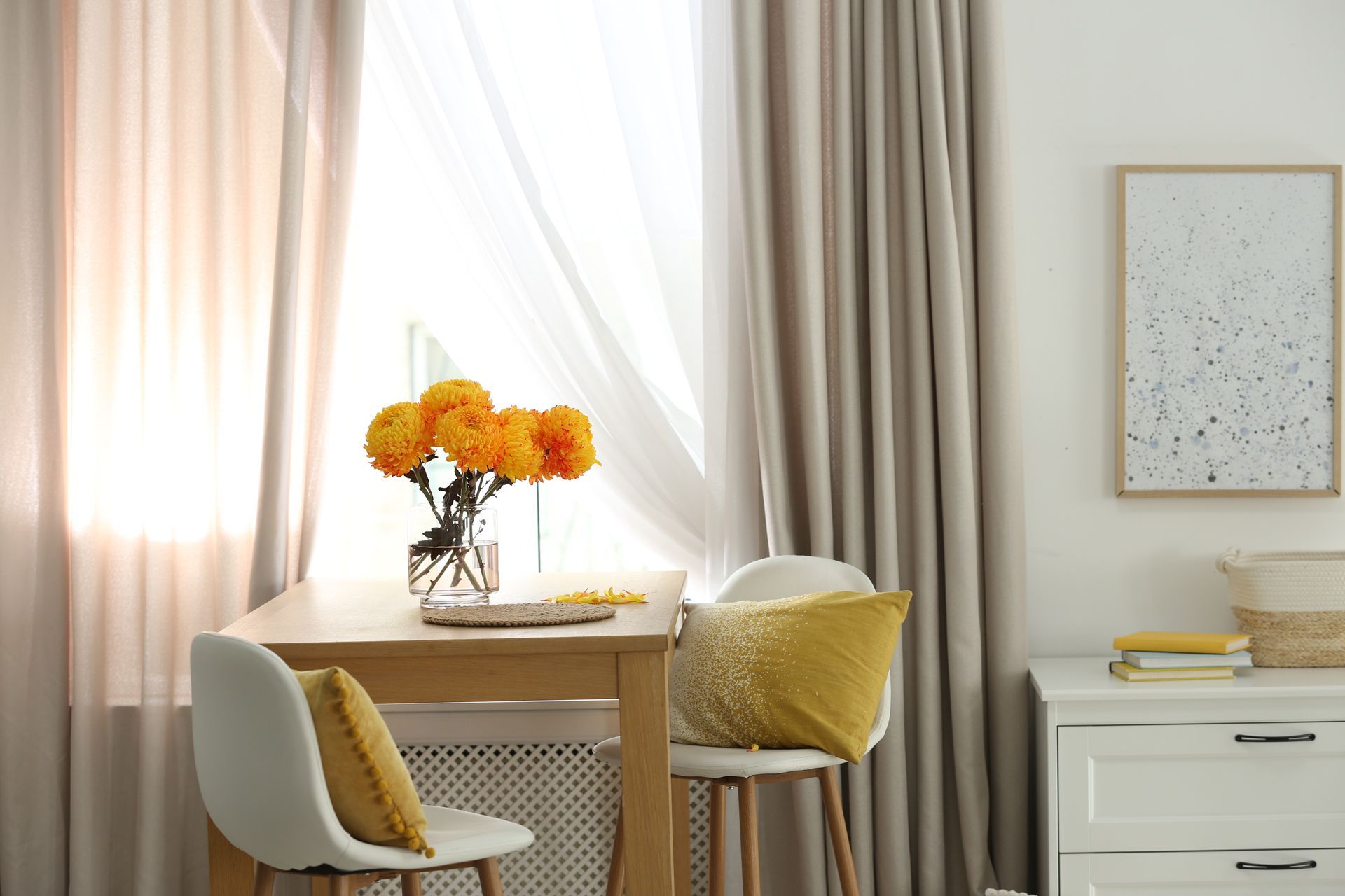 A bright interior scene with flowers on a table, soft curtains, and white furniture.