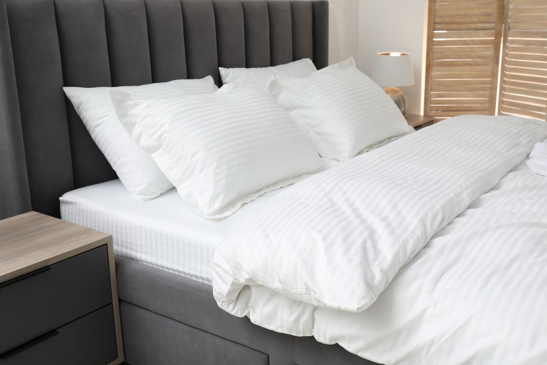 Bed with white bedding, pillows, and gray headboard. Side table visible.