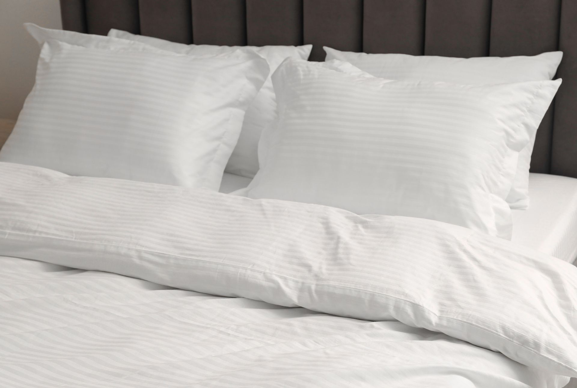 White bed with two pillows and a comforter, against a dark headboard.