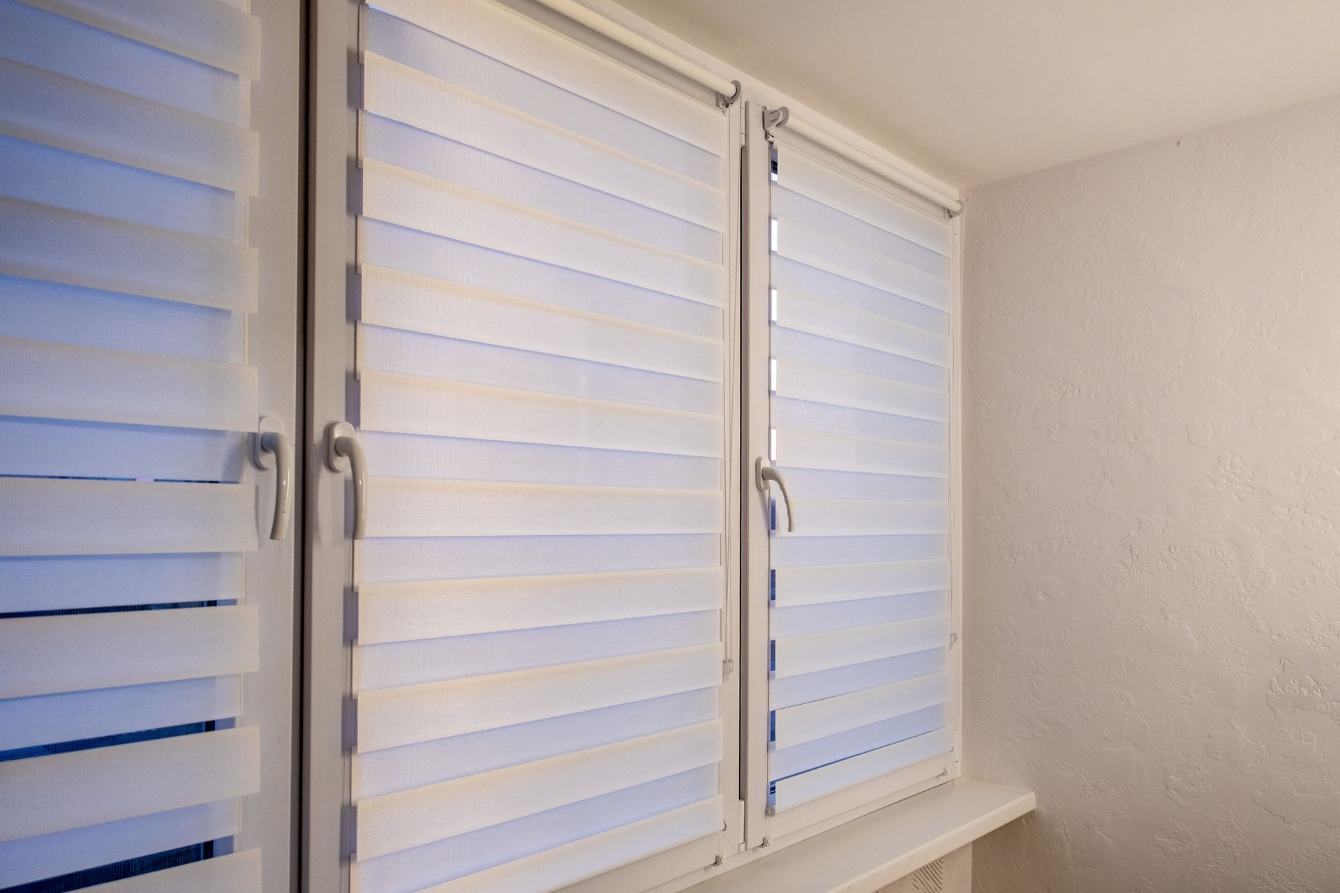 Wooden blinds filtering sunlight into a room, partially obscuring the view outside.