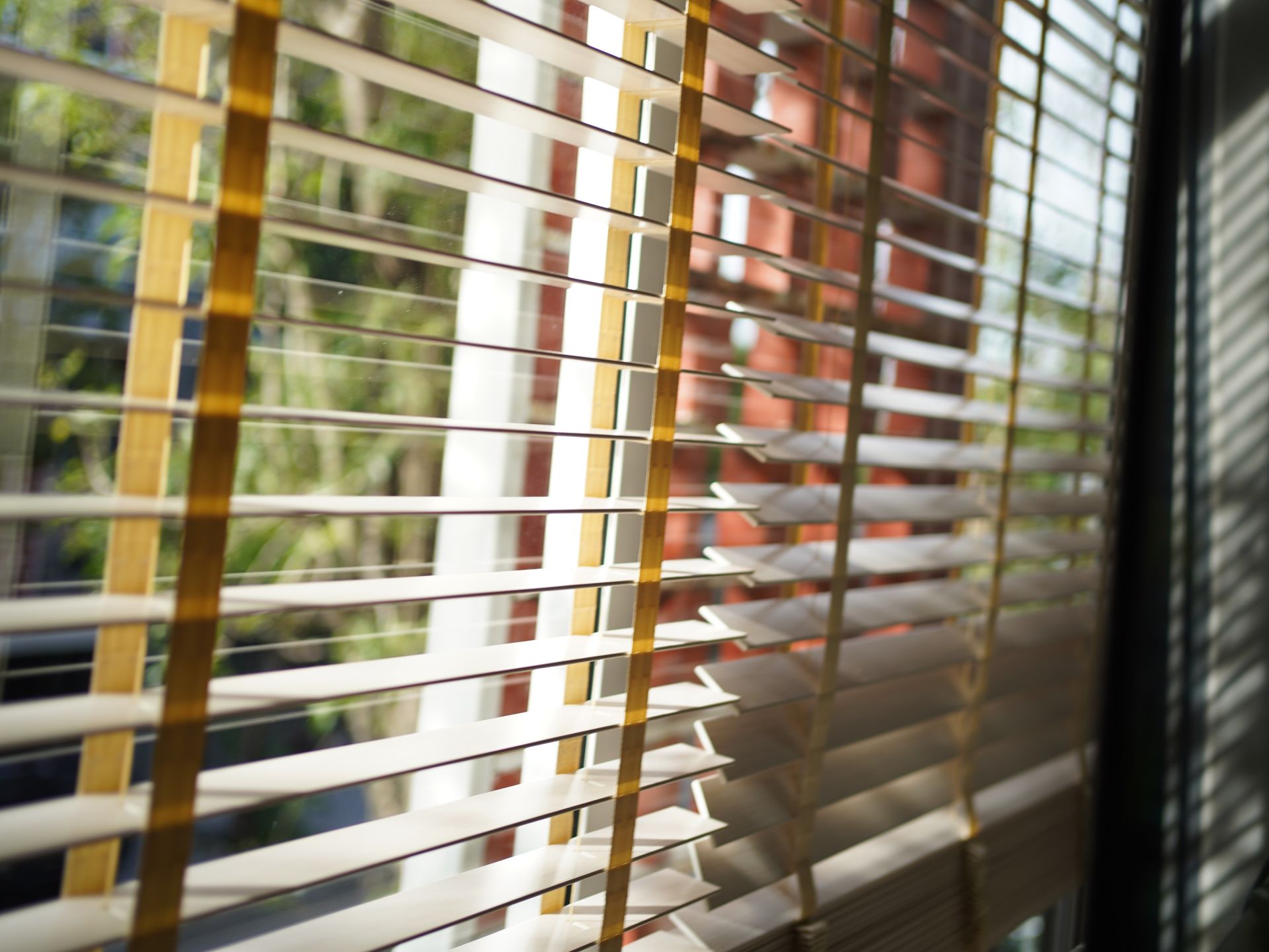 Wooden blinds filtering sunlight into a room, partially obscuring the view outside.