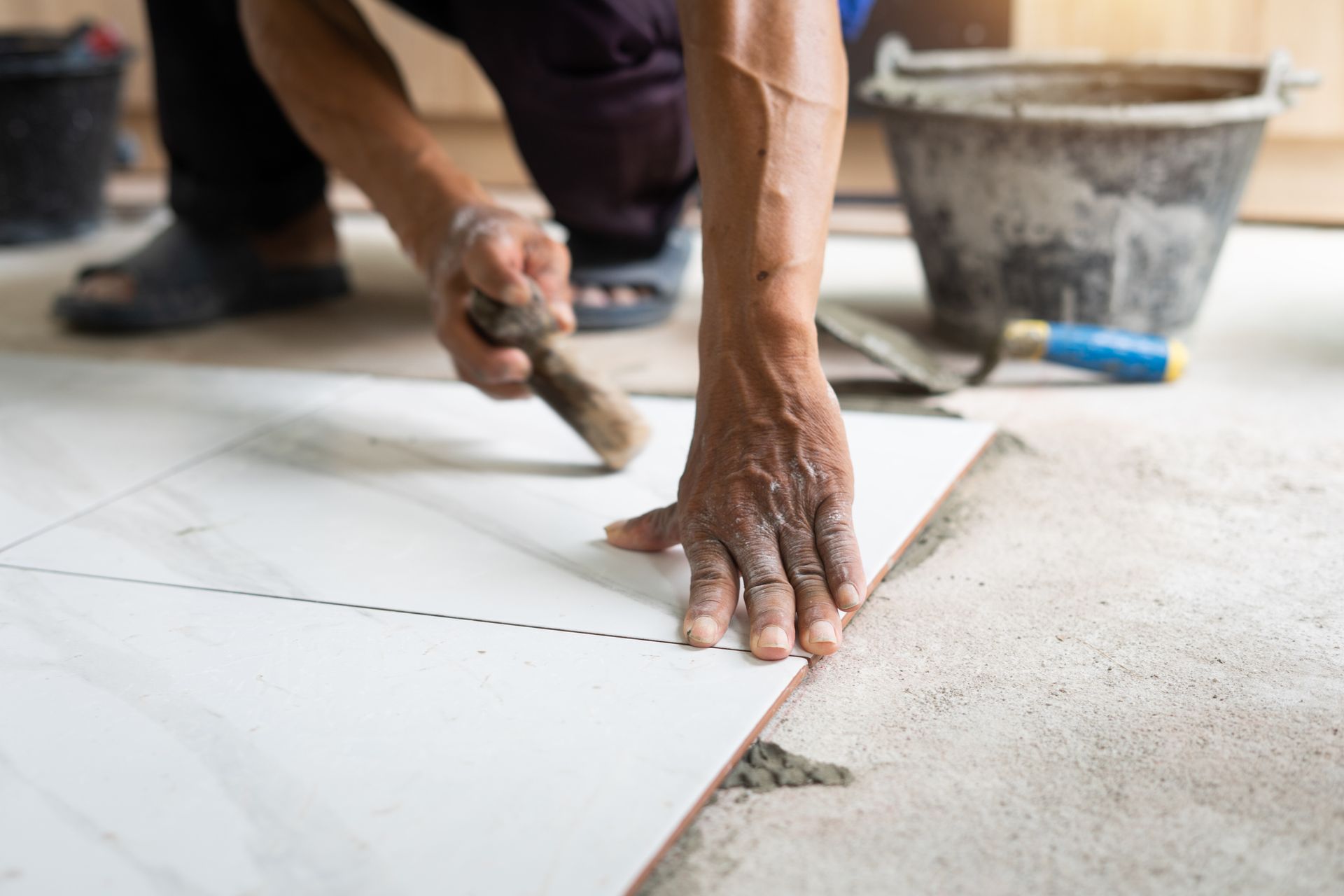 A man is laying tiles on the floor with a trowel.