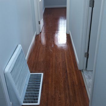 A hallway with hardwood floors and a white vent.