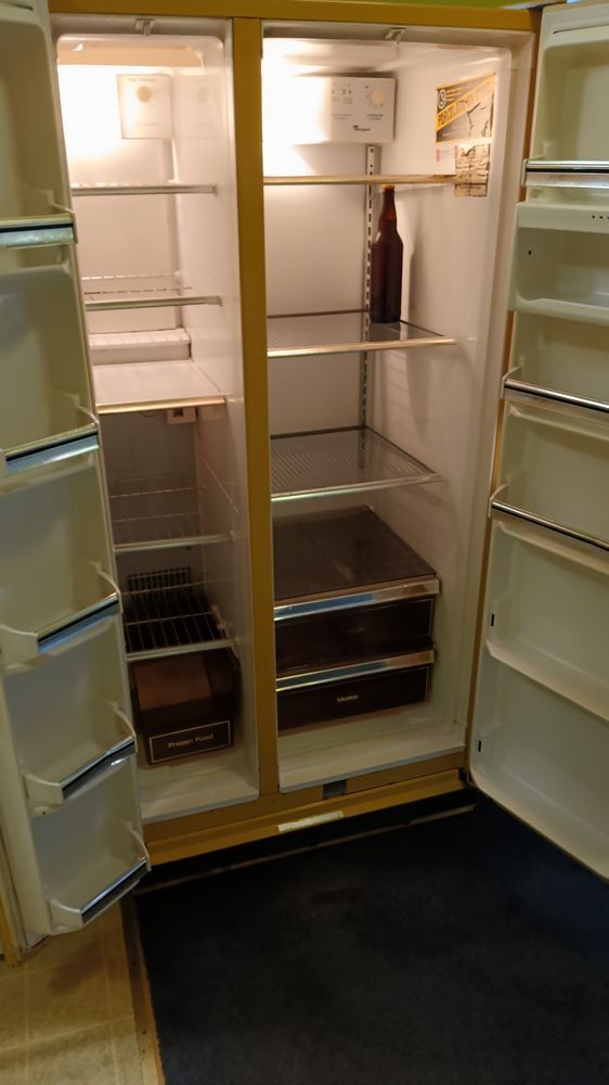 An empty refrigerator with its doors open and a bottle of wine on the shelf.