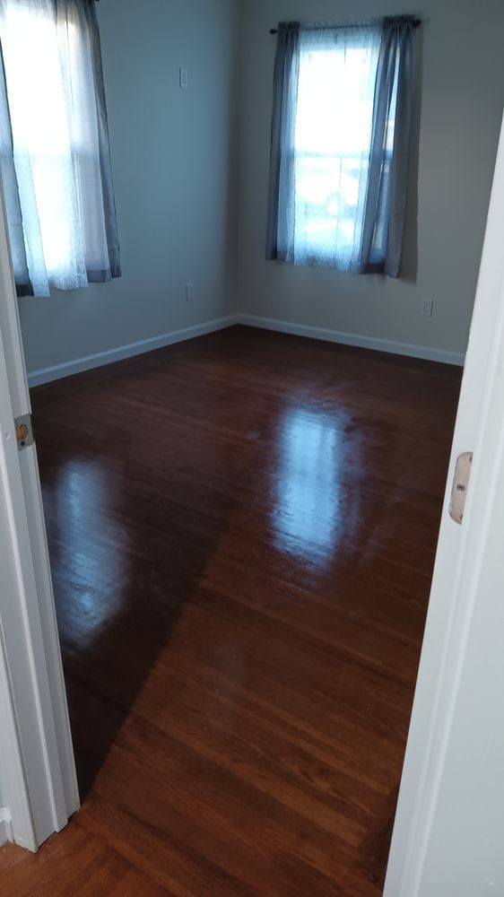 An empty room with hardwood floors and two windows.