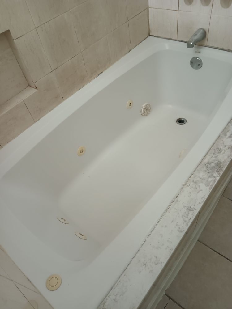 A white bathtub is sitting on a tiled counter in a bathroom.