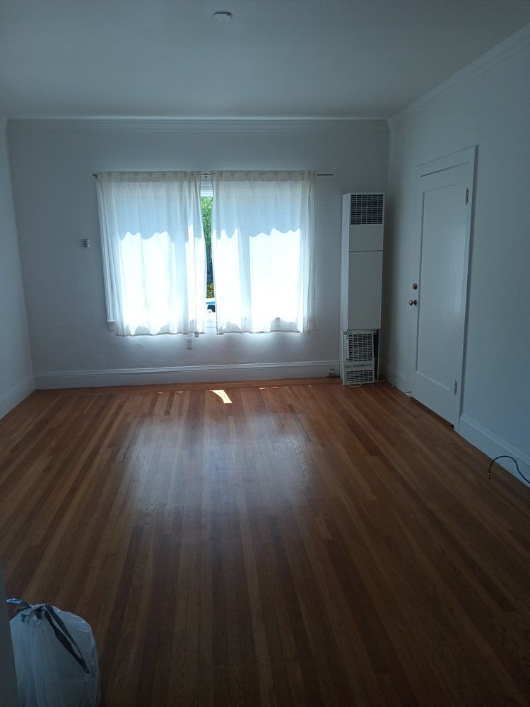 An empty living room with hardwood floors and white curtains