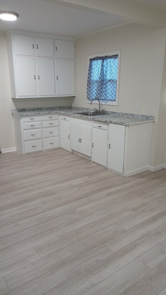 A kitchen with white cabinets , a sink , and a window.