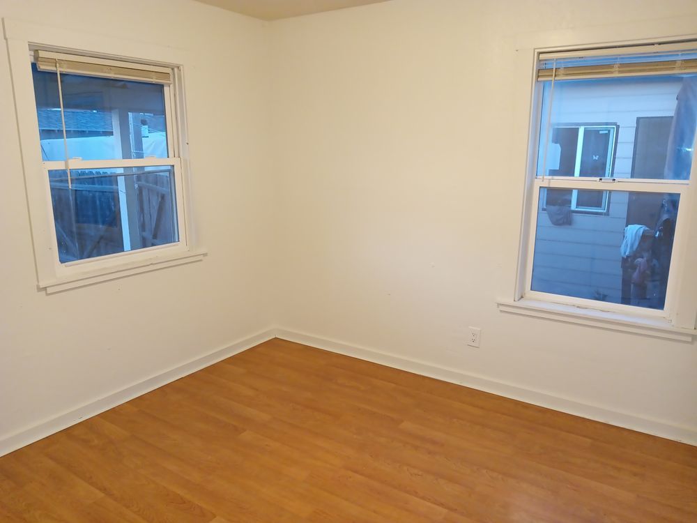 An empty room with hardwood floors and two windows