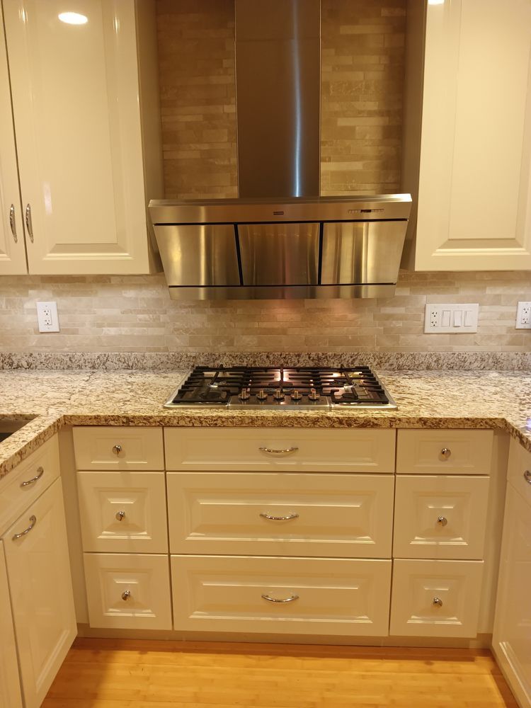 A kitchen with white cabinets , granite counter tops , and a stove top oven.