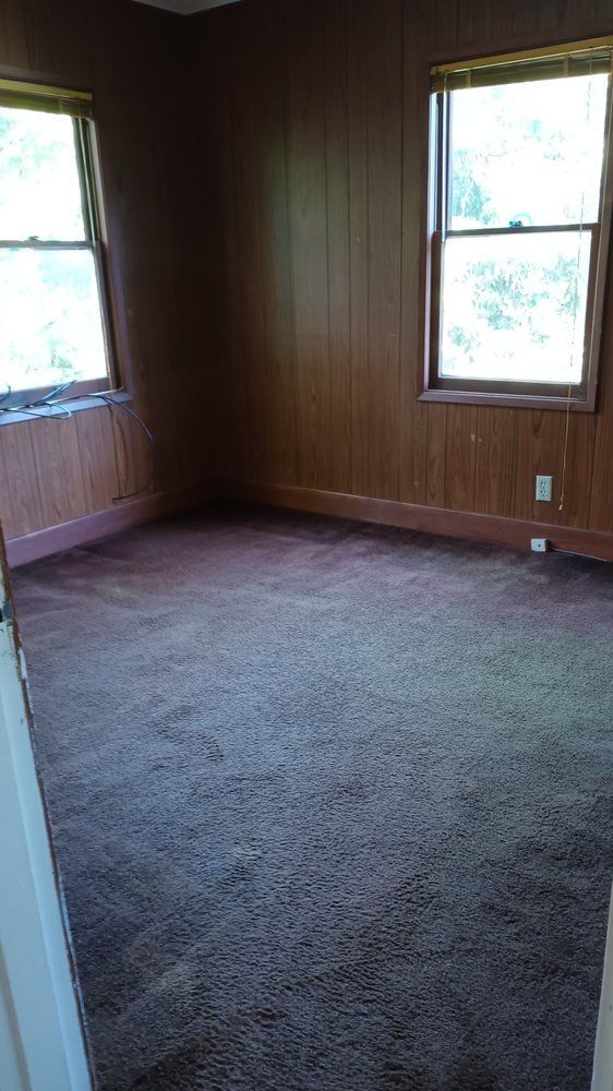 An empty room with wood paneling and a brown carpet.
