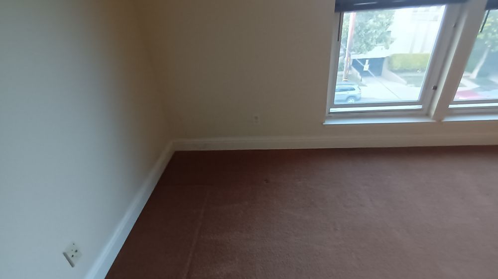 An empty room with a window and a brown carpet