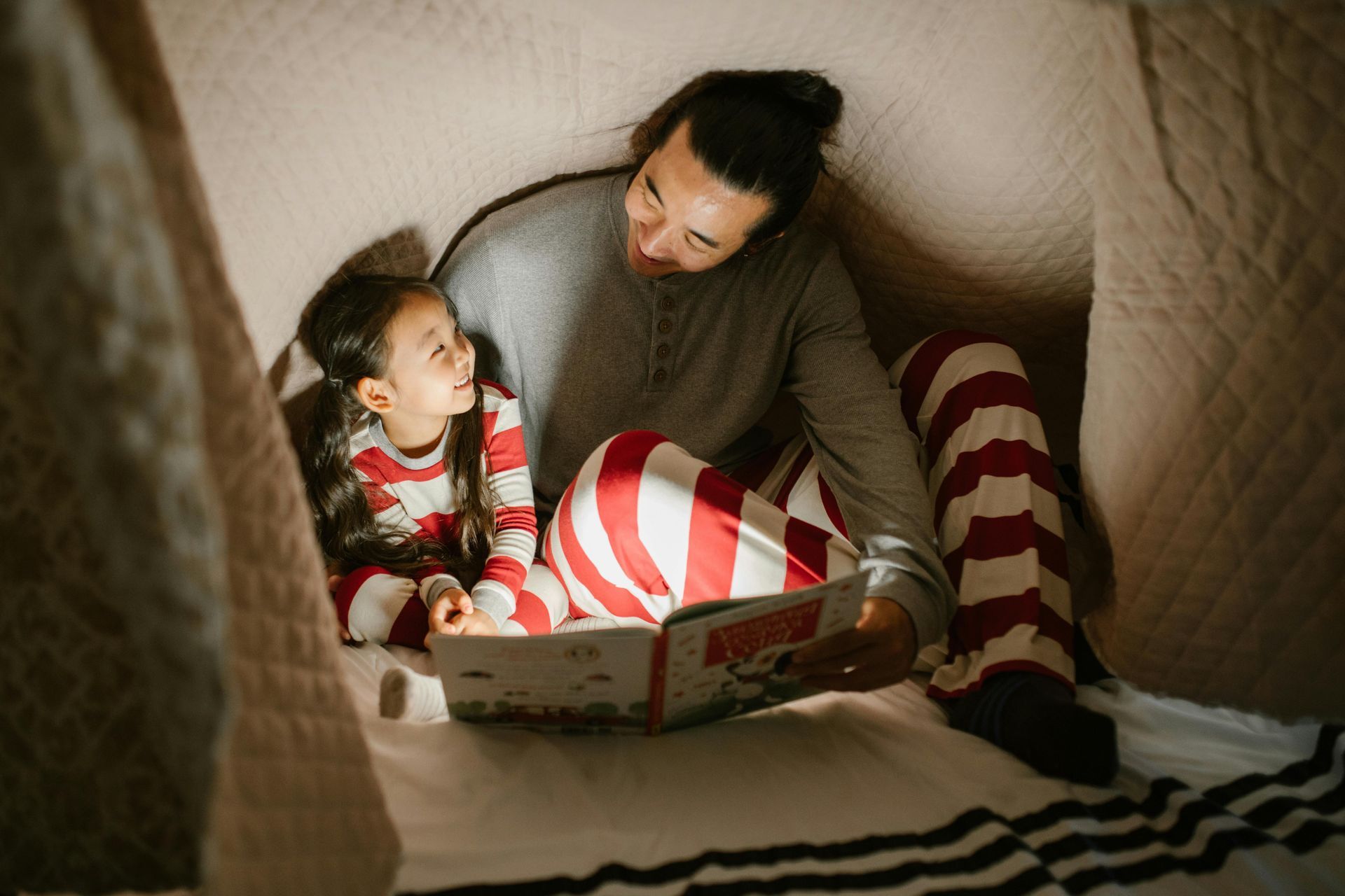 A man is reading a book to a little girl in a tent.