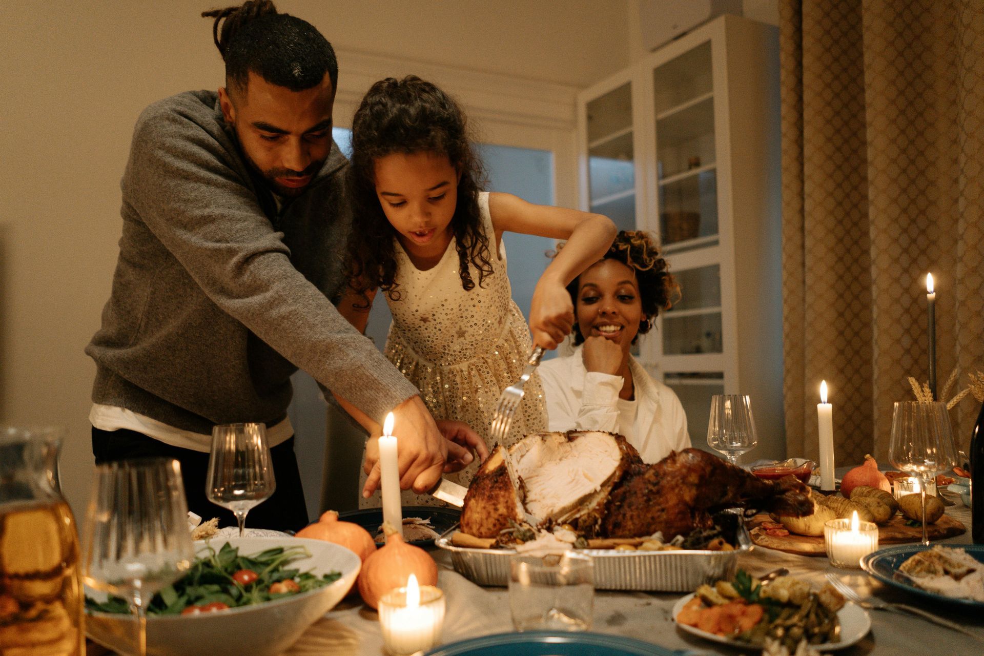 A man and two children are cutting a turkey at a dinner table.