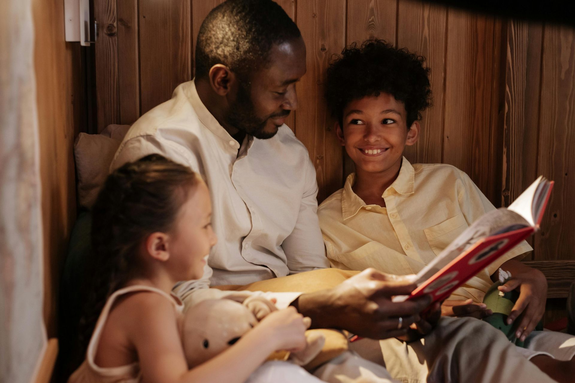 A man is reading a book to two children.