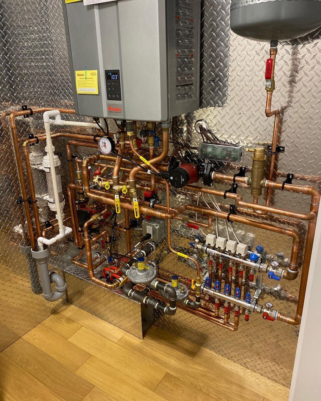 A room with a lot of copper pipes and a water heater.