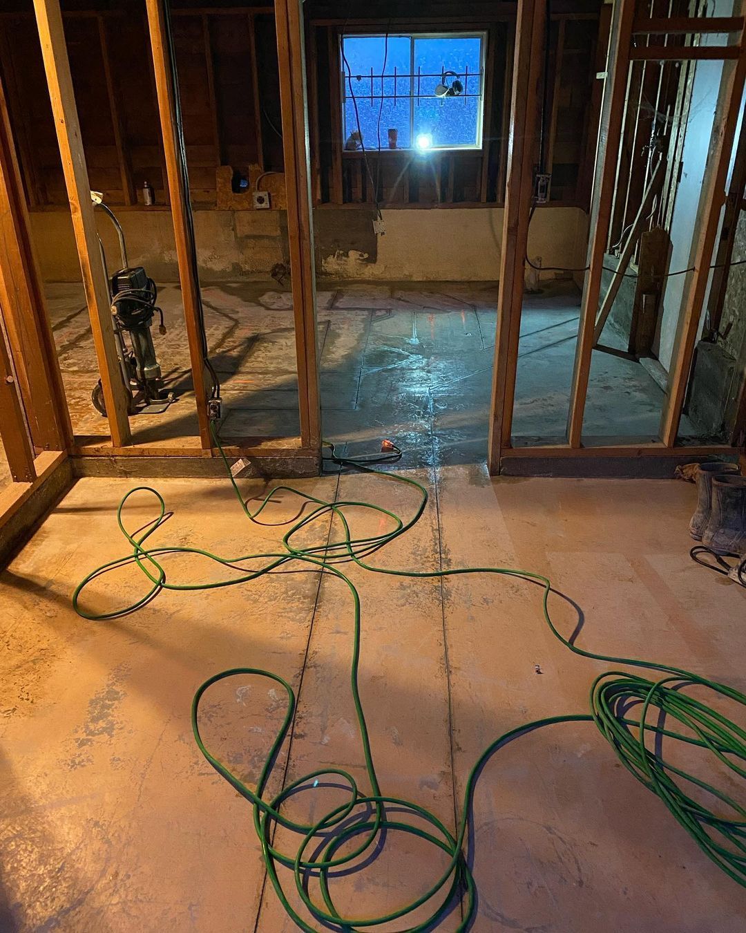 A green hose is laying on the floor in a room under construction.