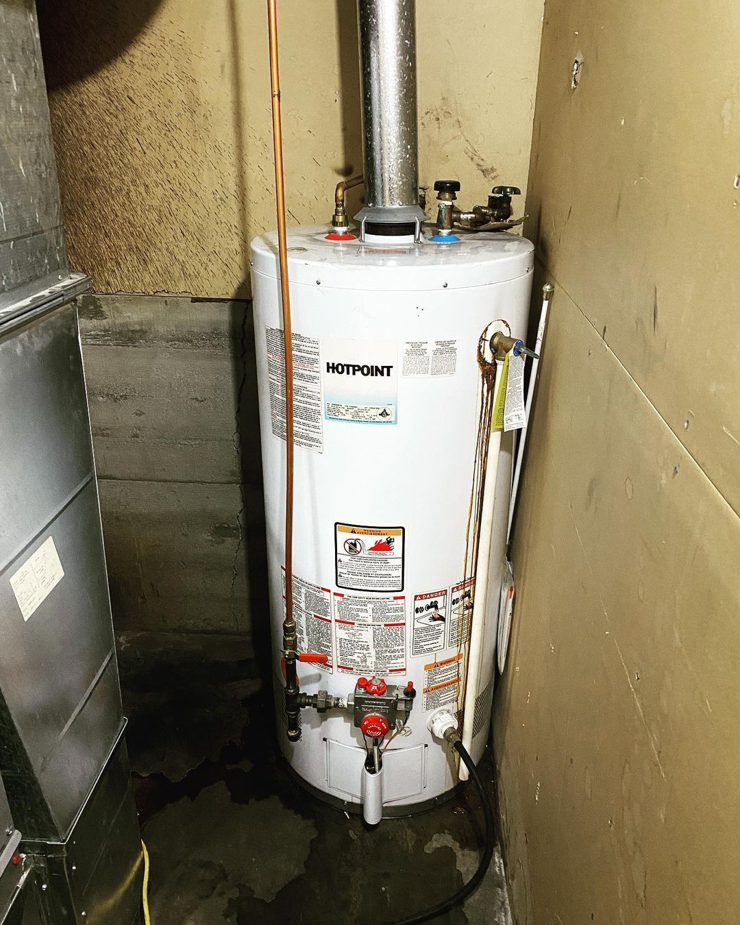 A white water heater is sitting in a corner of a room.