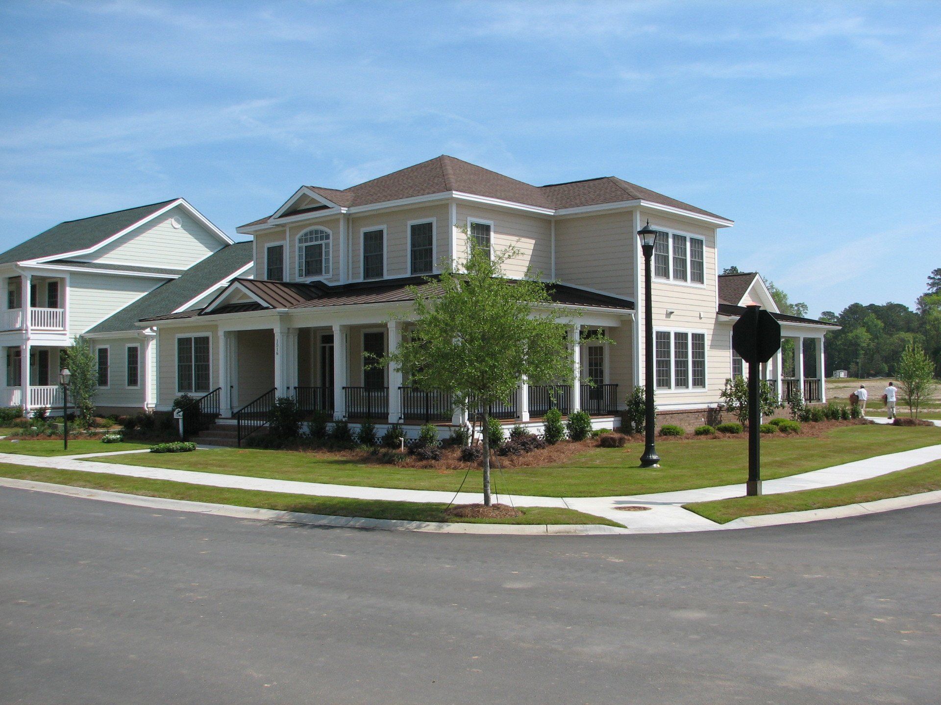 A large white house with a brown roof sits on the corner of a street