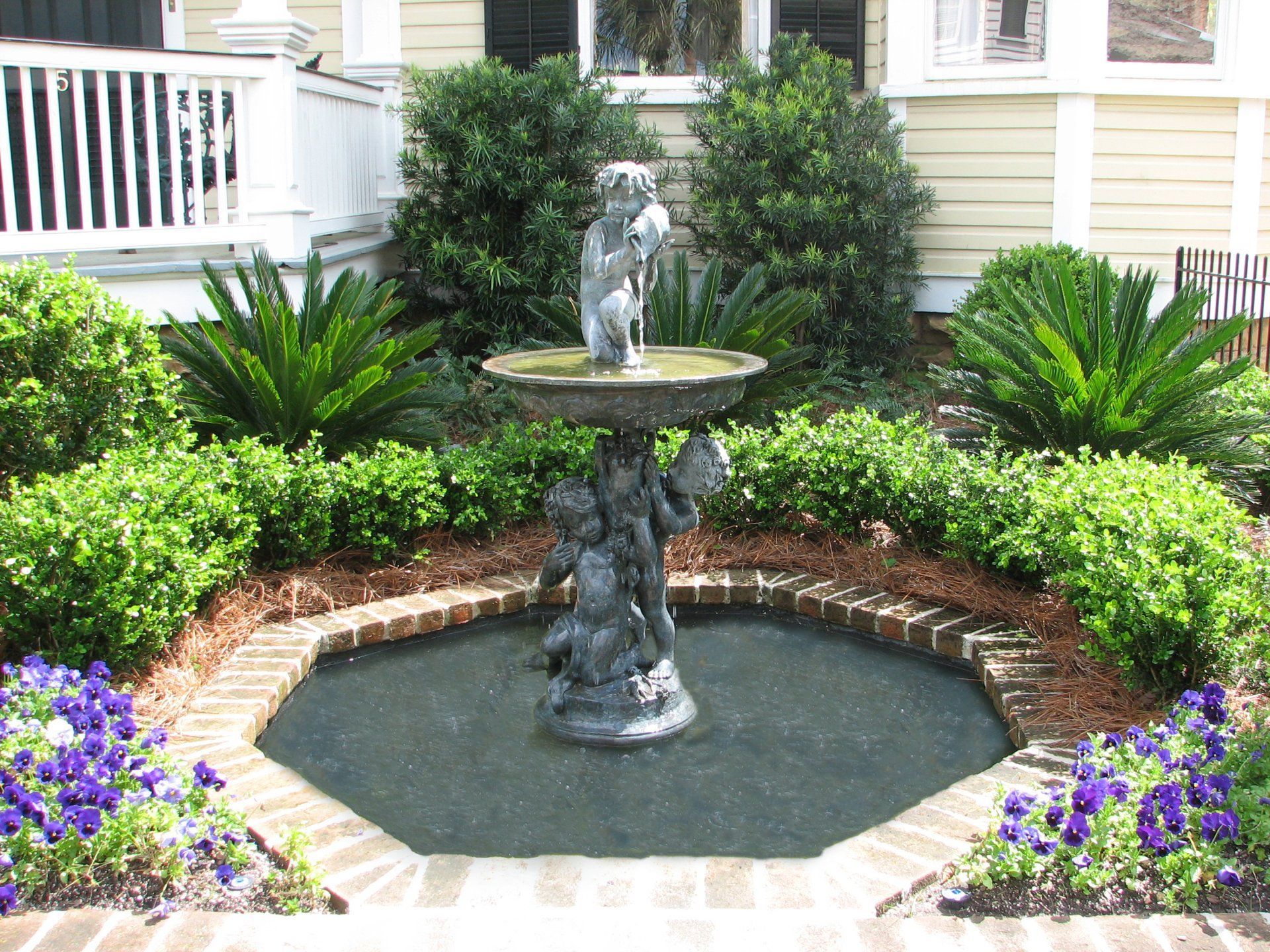 A fountain in the middle of a garden with purple flowers