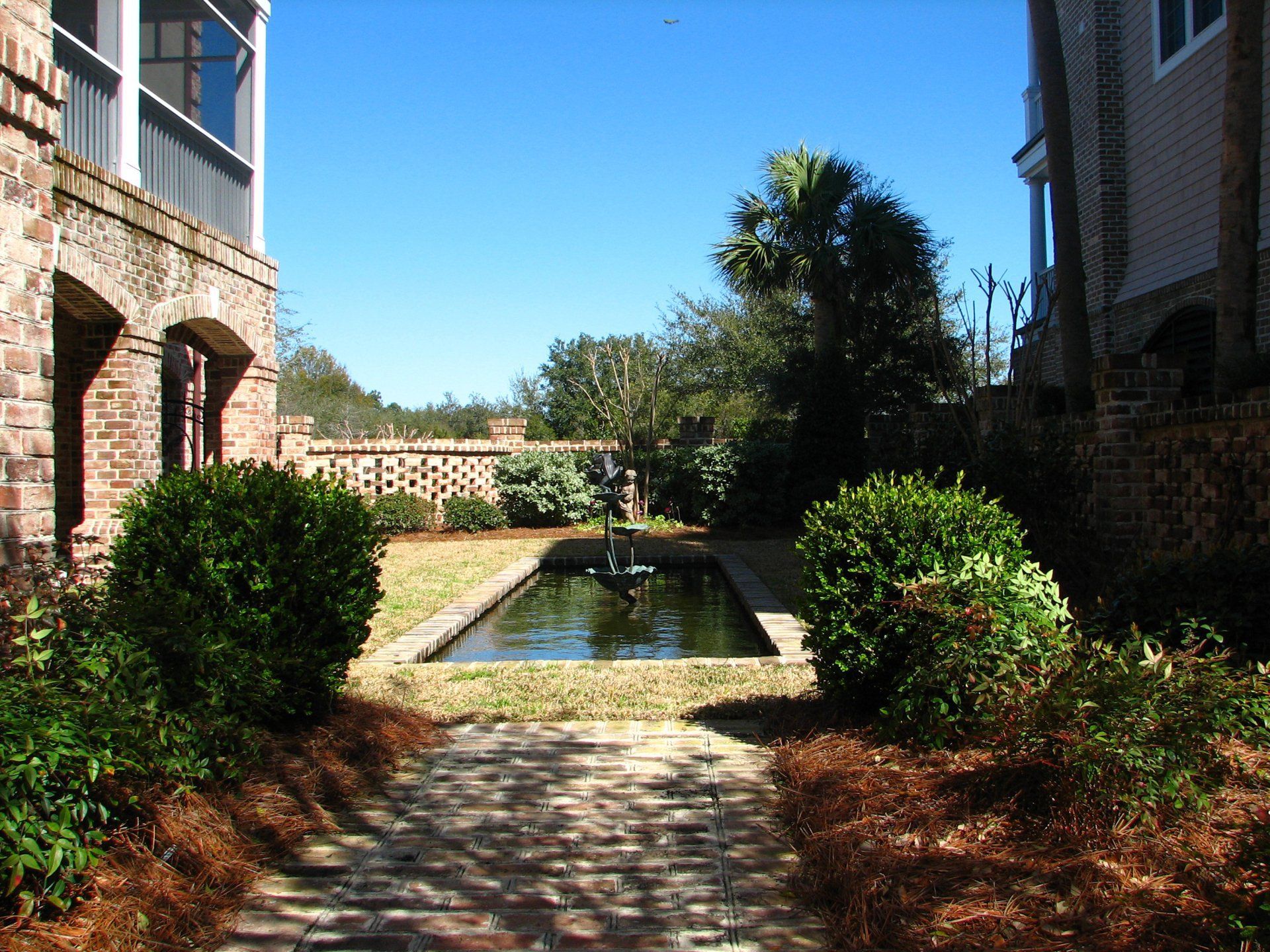 A brick walkway leads to a pond with a fountain in the middle