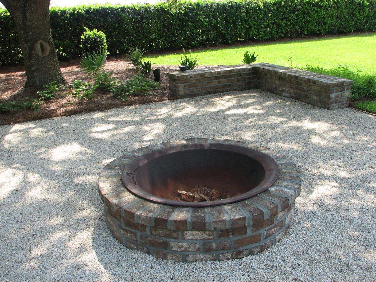 A fire pit made of bricks and gravel in a backyard