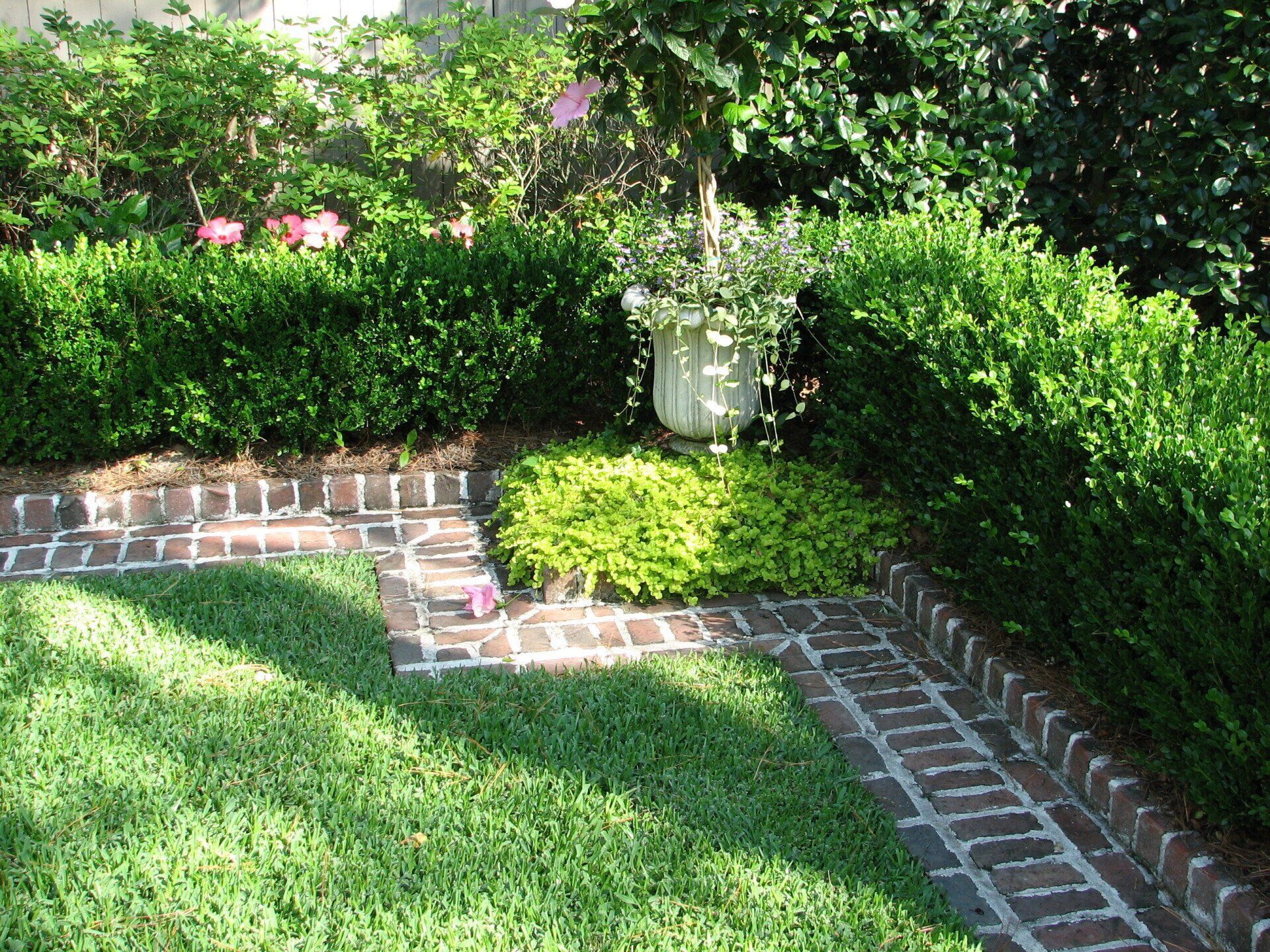 A brick walkway leading to a lush green garden