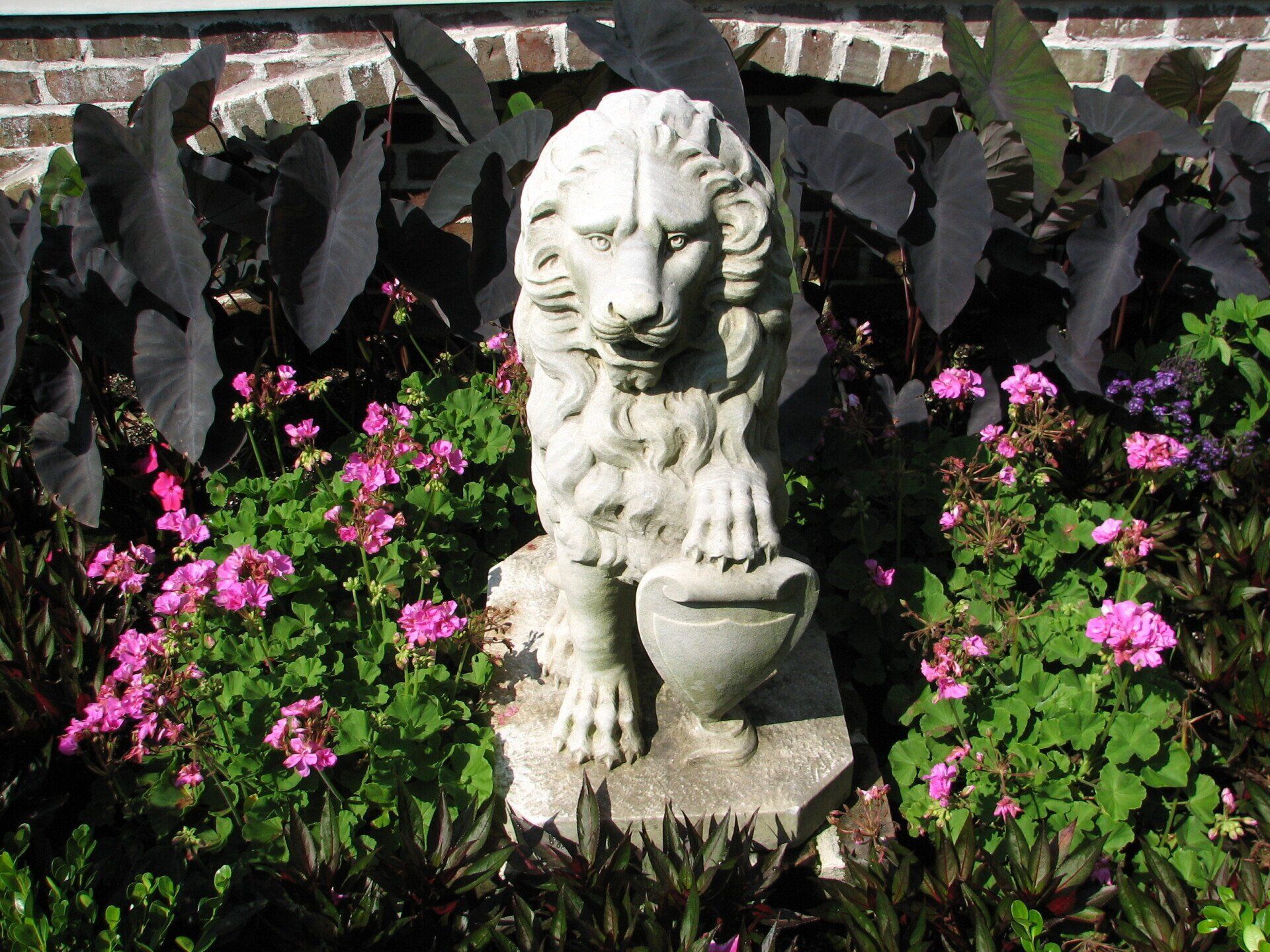 A statue of a lion sitting in a garden with pink flowers