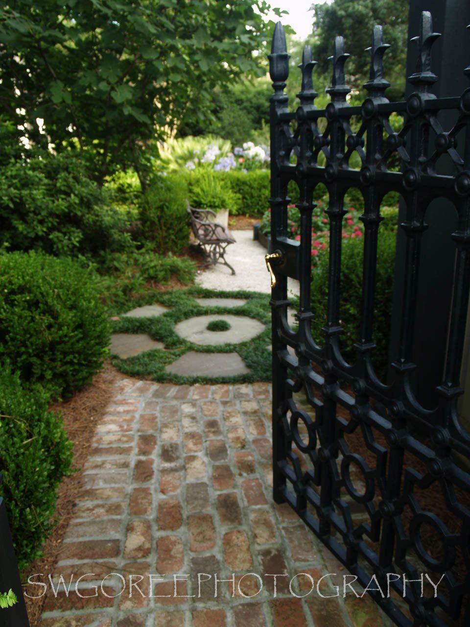 A black gate is open to a path in a garden
