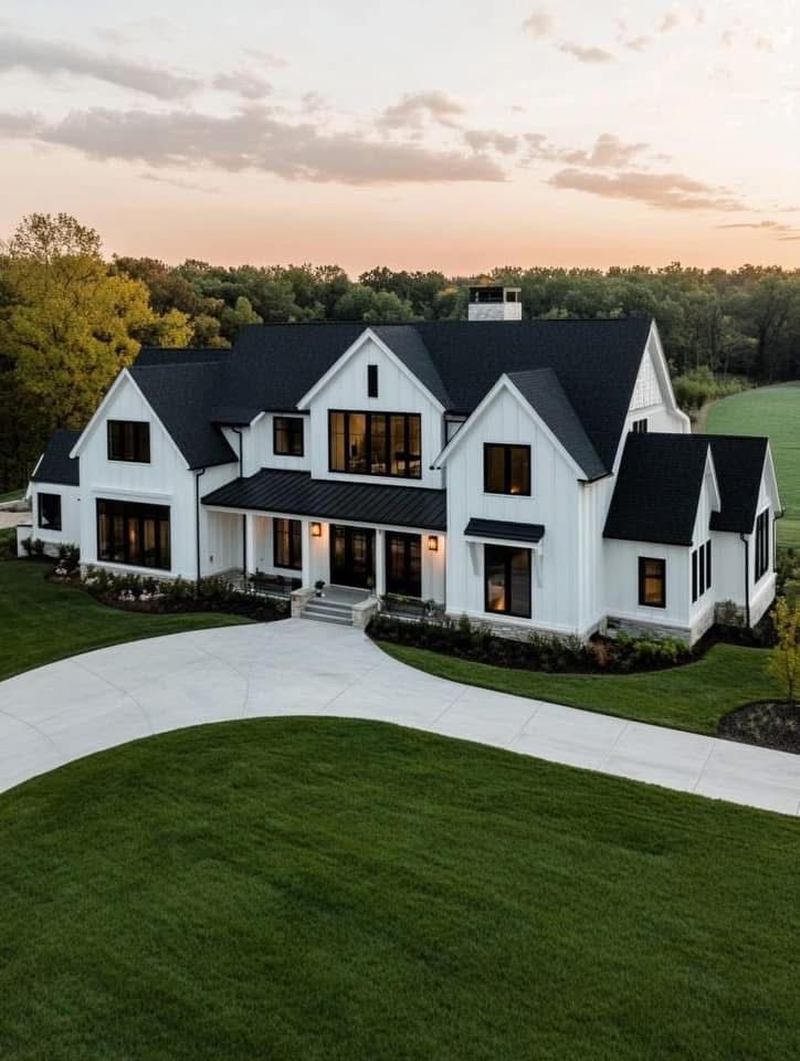 White farmhouse with black roof, large windows, and a curved driveway on a green lawn.