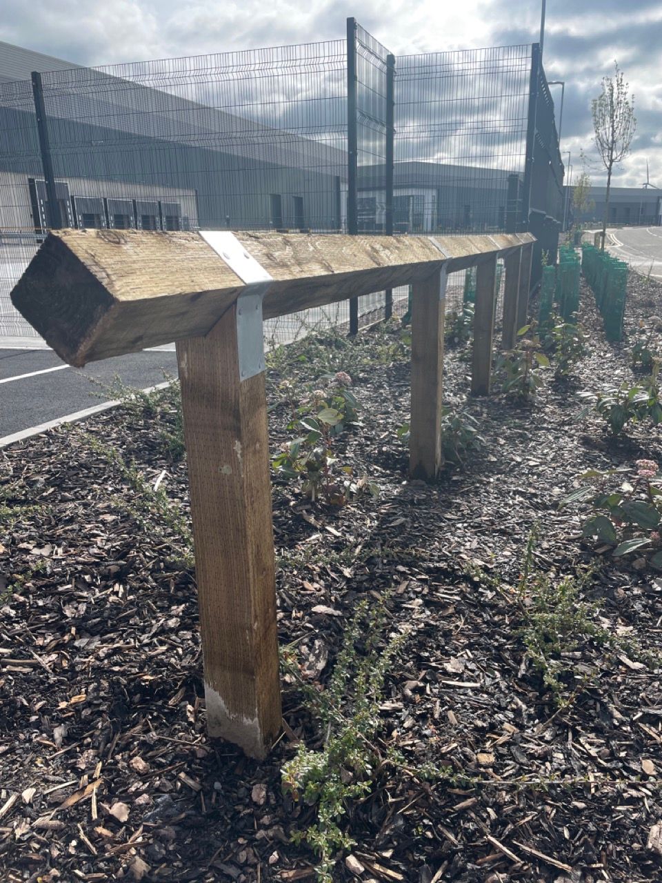 A wooden bench is sitting in the middle of a pile of mulch next to a fence.
