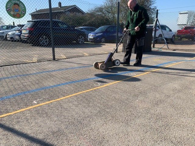 A man is using a lawn mower to cut a line on a tennis court.