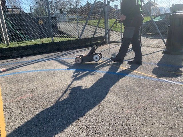 A man is using a machine to paint a line on a tennis court.