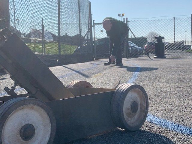 A man is using a machine to paint a blue line on the ground.
