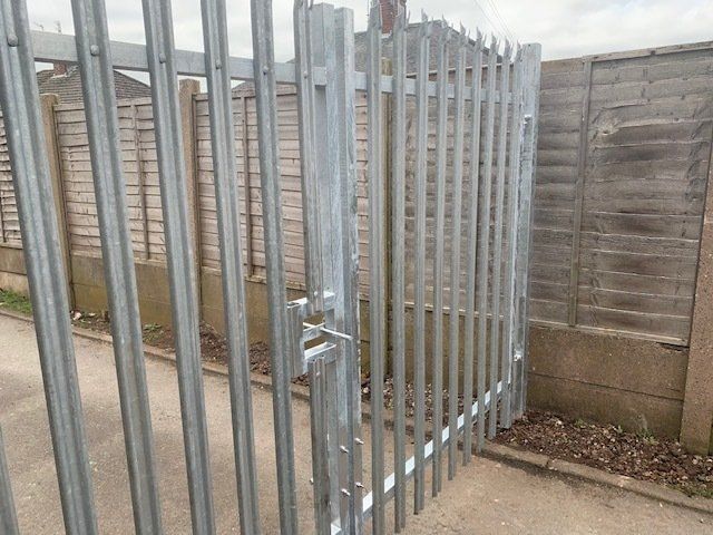 A metal fence with a broken gate and a wooden fence in the background.