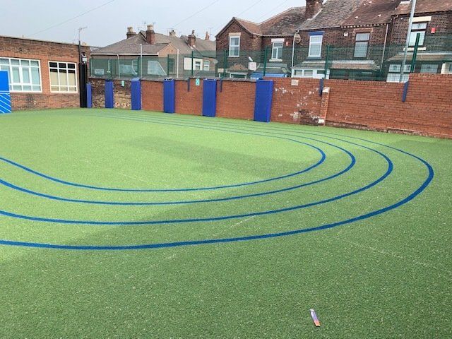 A green field with blue lines on it and houses in the background