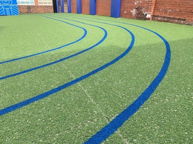 A green field with blue lines on it and a brick wall in the background.
