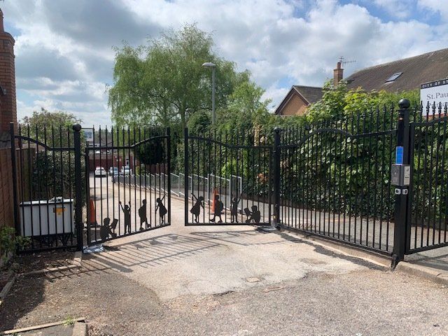 A wrought iron gate is open to a driveway.